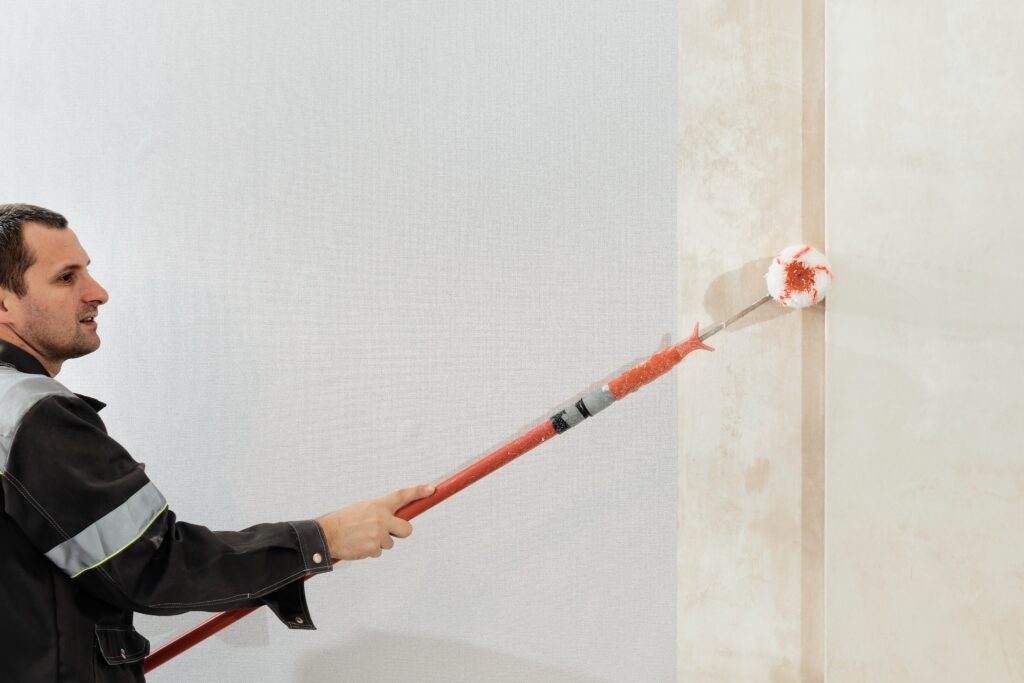 man worker applies glue with paint roller walls before wallpapering primer walls selective focus apartment renovation restoration idea indoors (1)